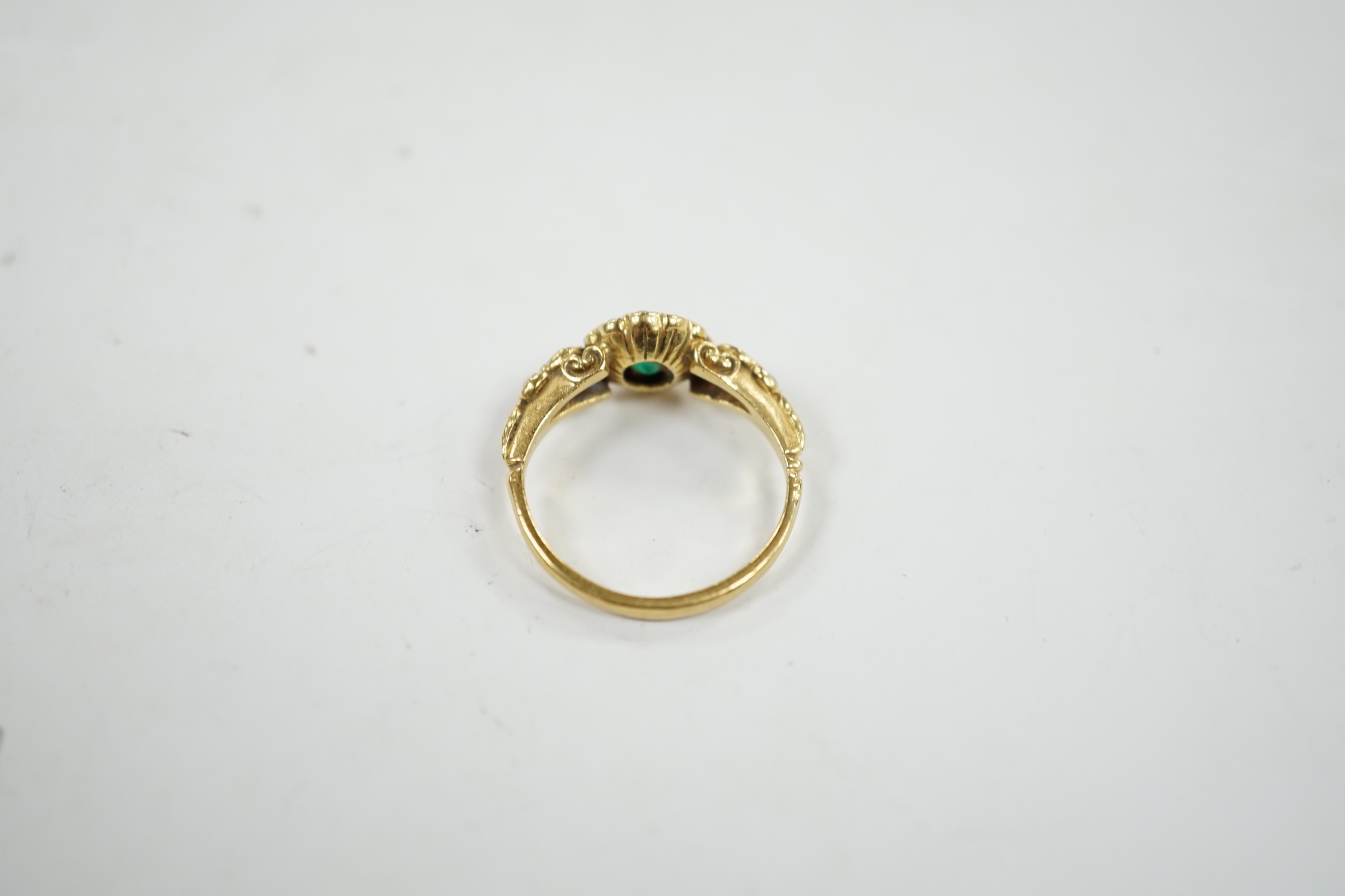 A Victorian style yellow metal emerald and diamond set circular cluster ring, with graduated diamond set shoulders, size N, gross weight 3.7 grams.
